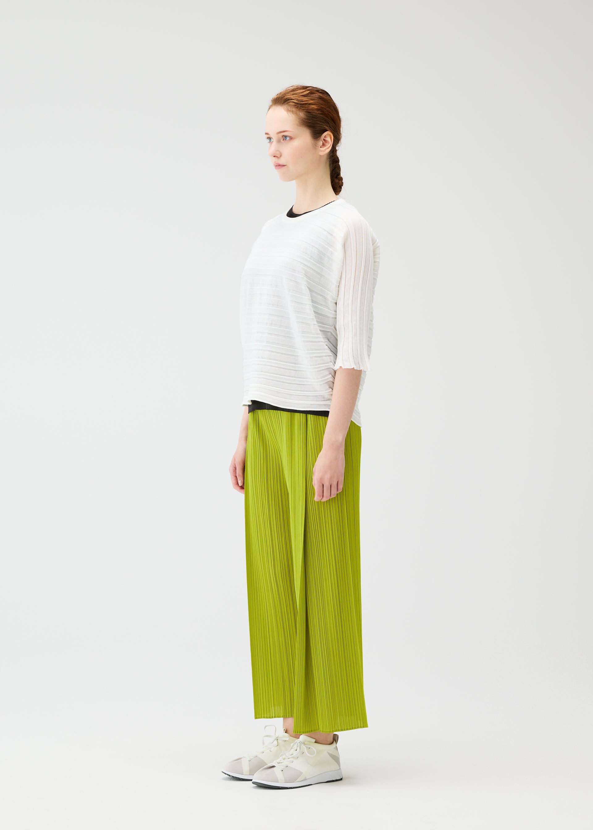 Zoomed view A woman with braided hair stands in profile against a white background, wearing the PLEATS PLEASE ISSEY MIYAKE STEP KNIT white top and lime green pleated wide-leg pants—an effortless summer look completed with white sneakers.