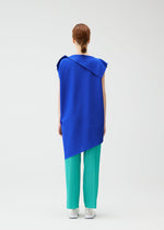 A person with red hair in a low bun faces away, wearing the PLEATS PLEASE ISSEY MIYAKE A-POC SEA GLASS sleeveless royal blue tunic over pleated turquoise pants and white shoes against a plain white background.