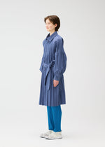A person stands sideways wearing a long-sleeved, belted SMOOTH COAT by PLEATS PLEASE ISSEY MIYAKE, blue pleated pants, and white shoes against a plain white background.