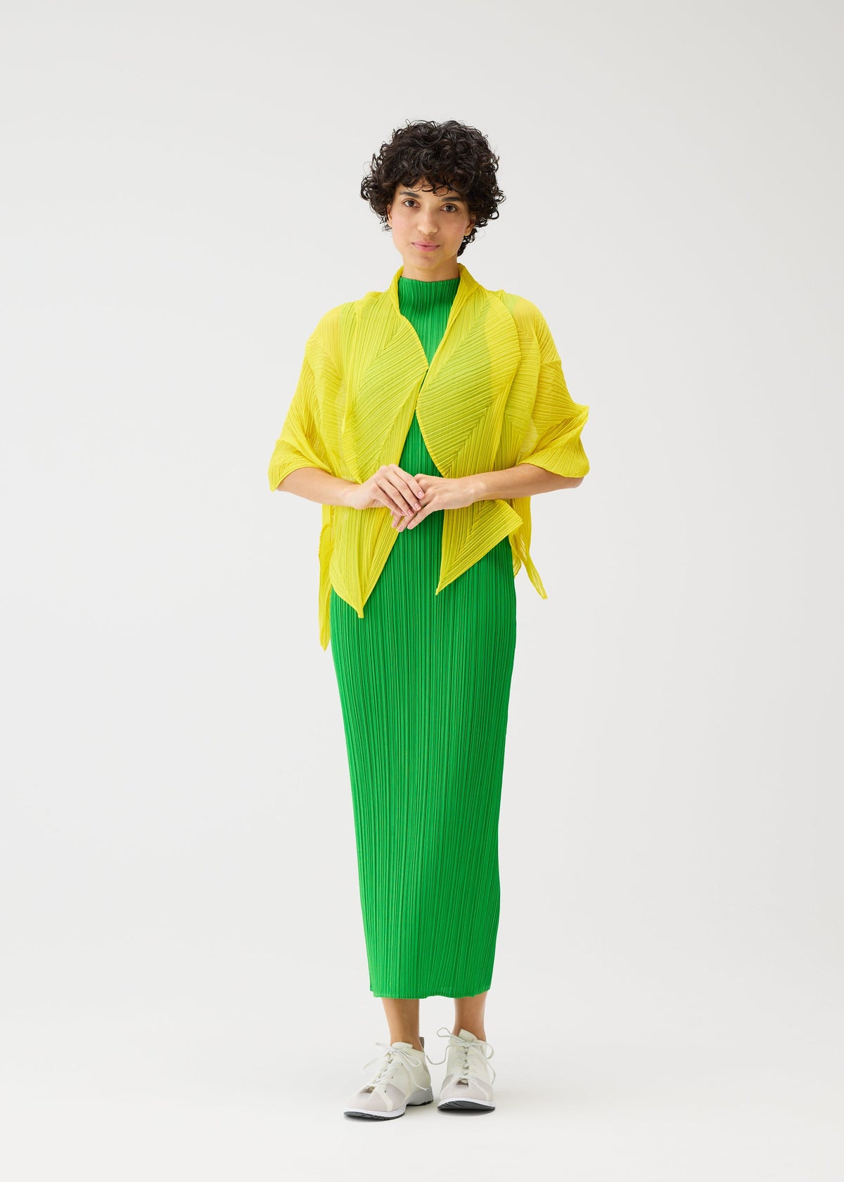 A person stands against a white backdrop wearing a bright green, pleated, ankle-length dress, a yellow textured jacket, and white sneakers. Their short curly hair is adorned with the PLEATS PLEASE ISSEY MIYAKE ZIGZAG SCARF for extra charm. view 7 of 7