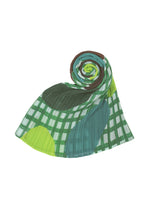 The MARKET MADAME-T pleated stole by PLEATS PLEASE ISSEY MIYAKE features a green and white checkered pattern with teal and lime paper-cut inspired shapes, rolled into a spiral at one end against a white background.