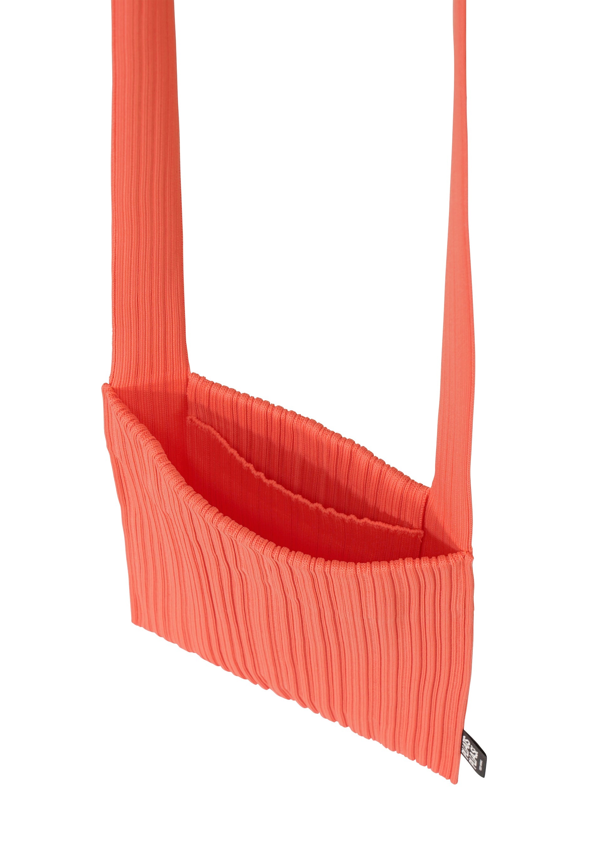 Zoomed view The CREPE KNIT BAG by PLEATS PLEASE ISSEY MIYAKE is a bright coral, pleated fabric bag with a wide strap, curved rectangular shape, and a small black tag at the bottom side. Shown against a white background.