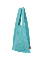 The PLEATS SHOPPING TOTE by PLEATS PLEASE ISSEY MIYAKE is a turquoise pleated bag with two handles and a small black label near the bottom, shown against a white background.