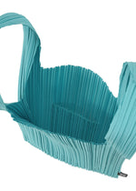 The PLEATS SHOPPING TOTE by PLEATS PLEASE ISSEY MIYAKE is a turquoise, pleated bag featuring a wide strap, open top, spacious textured interior, and a small inner pocket.