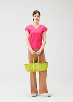A person stands against a plain background wearing a bright pink, short-sleeve, pleated top, brown pleated pants, white shoes, and holding the PLEATS PLEASE ISSEY MIYAKE PLEATS BOSTON BAG in lime green with both hands.