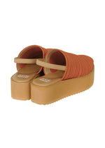The PLEATS KNIT SANDALS by PLEATS PLEASE ISSEY MIYAKE are orange ribbed slip-on platform sandals with thick beige soles and pleats, displayed from the back and side on a white background.
