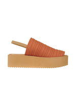 A side view of the PLEATS PLEASE ISSEY MIYAKE PLEATS KNIT SANDALS shows a tan platform, thick sole, orange textured pleated upper, and a slim beige back strap.