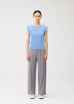 A woman stands facing forward against a plain white background, wearing the MIST AUGUST light blue round-neck top with French sleeves and gray wide-leg pleated pants from PLEATS PLEASE ISSEY MIYAKE, paired with white sneakers.