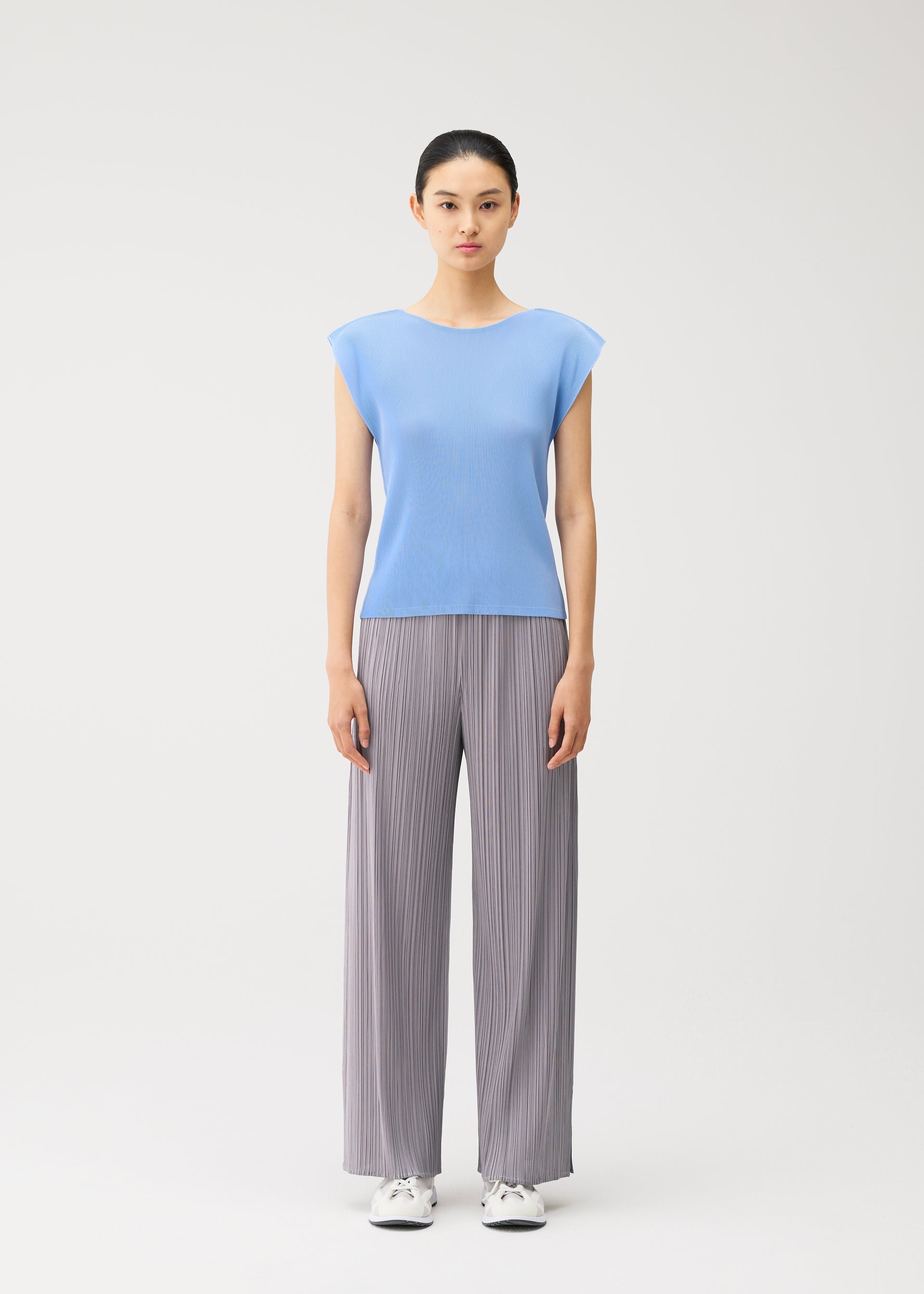 Zoomed view A woman stands facing forward against a plain white background, wearing the MIST AUGUST light blue round-neck top with French sleeves and gray wide-leg pleated pants from PLEATS PLEASE ISSEY MIYAKE, paired with white sneakers.