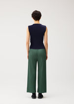 A person with short dark hair is seen from behind, wearing the MIST SEPTEMBER lightweight high-neck sleeveless navy top and loose green finely pleated pants by PLEATS PLEASE ISSEY MIYAKE, standing against a plain white background.
