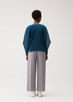 Wearing the TATAMI AUGUST wide-leg, light gray pleated pants from PLEATS PLEASE ISSEY MIYAKE, a person stands facing away in a loose teal sweater and crisp white shoes against a plain white background, effortlessly pairing cool tones and airy textures.