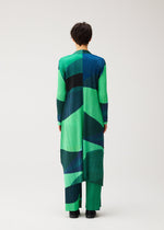 A person stands with their back to the camera, modeling the ORBIT long coat by PLEATS PLEASE ISSEY MIYAKE, featuring sheer colors and an abstract pattern of green, blue, and black shapes on a plain light background.