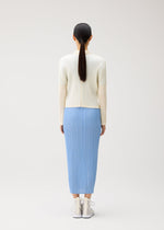 Wearing pieces from PLEATS PLEASE ISSEY MIYAKE’s MONTHLY COLORS: AUGUST collection, a person stands facing away in a cream ribbed top and light blue pleated skirt, paired with white sneakers. Their straight black hair is tied back in a low ponytail. The crisp color palette stands out against the plain, light background for a fresh midsummer effect.