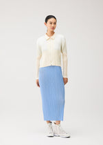 A person stands against a plain background wearing the MONTHLY COLORS : AUGUST cream-colored zippered cardigan from PLEATS PLEASE ISSEY MIYAKE, layered over a light blue pleated skirt, and paired with white high-top sneakers.