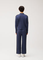 A person faces away, wearing PLEATS PLEASE ISSEY MIYAKE COTTON DENIM: a matching dark blue ribbed sweater and wide-leg pants with a cotton collared jacket and white shoes, set against a plain light background.