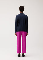 A person with short curly hair is standing facing away on a plain light background, wearing the PLEATS PLEASE ISSEY MIYAKE PLEATS JACKET in navy paired with vibrant pink pleated wide-leg pants and black shoes.