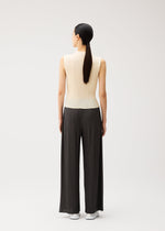 A person stands facing away, wearing the MONTHLY COLORS : AUGUST sleeveless, cream-colored top and loose, black pleated straight pants from PLEATS PLEASE ISSEY MIYAKE, paired with white shoes. Their straight, dark hair is tied in a low ponytail. Perfect for summer wear, this ensemble by PLEATS PLEASE ISSEY MIYAKE features striking colors that stand out against the plain, light background.