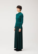 A person in profile wears MONTHLY COLORS : OCTOBER by PLEATS PLEASE ISSEY MIYAKE—a teal, long-sleeved ribbed top and matching pleated skirt with black shoes against a plain light background.