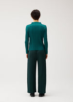 Person stands with their back to the camera, wearing MONTHLY COLORS : OCTOBER by PLEATS PLEASE ISSEY MIYAKE—wide-leg pleated pants and matching green pleated top—paired with black shoes against a plain light background.