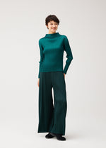A person stands against a plain background, smiling and looking to the side, wearing the teal MONTHLY COLORS : OCTOBER set by PLEATS PLEASE ISSEY MIYAKE with black shoes.