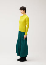 A woman with short dark hair smiles sideways, wearing the MONTHLY COLORS : OCTOBER by PLEATS PLEASE ISSEY MIYAKE—a bright yellow ribbed turtleneck sweater and flared pants against a plain white background.