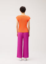 A person stands facing away, wearing an orange short-sleeve top, THICKER BOTTOMS 2 wide-leg pants by PLEATS PLEASE ISSEY MIYAKE in bright pink with pockets, and white shoes, against a plain light background.