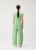 A person with long dark hair in a ponytail is seen from behind, standing against a plain white background and wearing the PLEATS PLEASE ISSEY MIYAKE FOLD set—a light green, pleated sleeveless top paired with matching wide-leg, flared pants featuring a distinctive design.