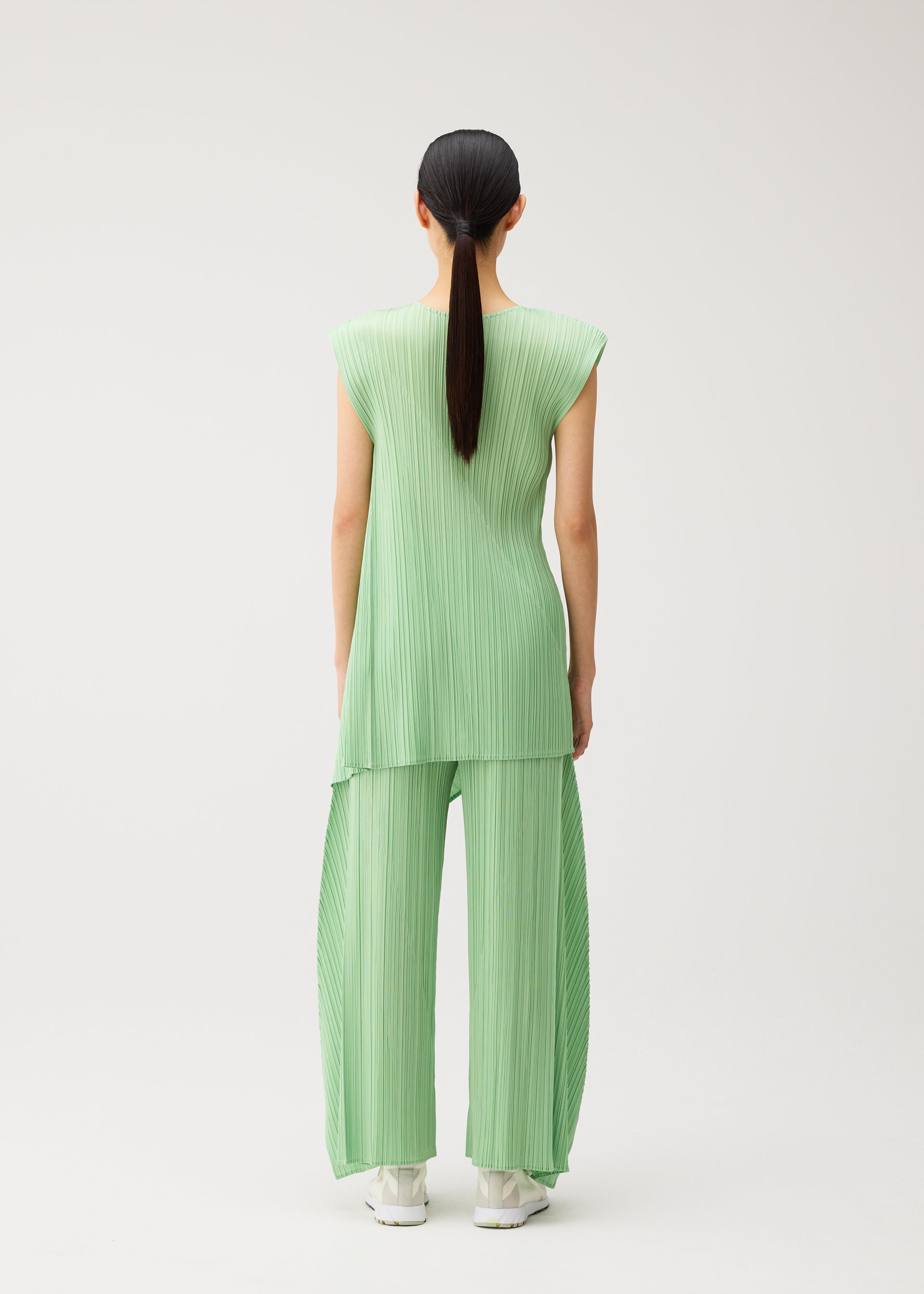 Zoomed view A person with long dark hair in a ponytail is seen from behind, standing against a plain white background and wearing the PLEATS PLEASE ISSEY MIYAKE FOLD set—a light green, pleated sleeveless top paired with matching wide-leg, flared pants featuring a distinctive design.