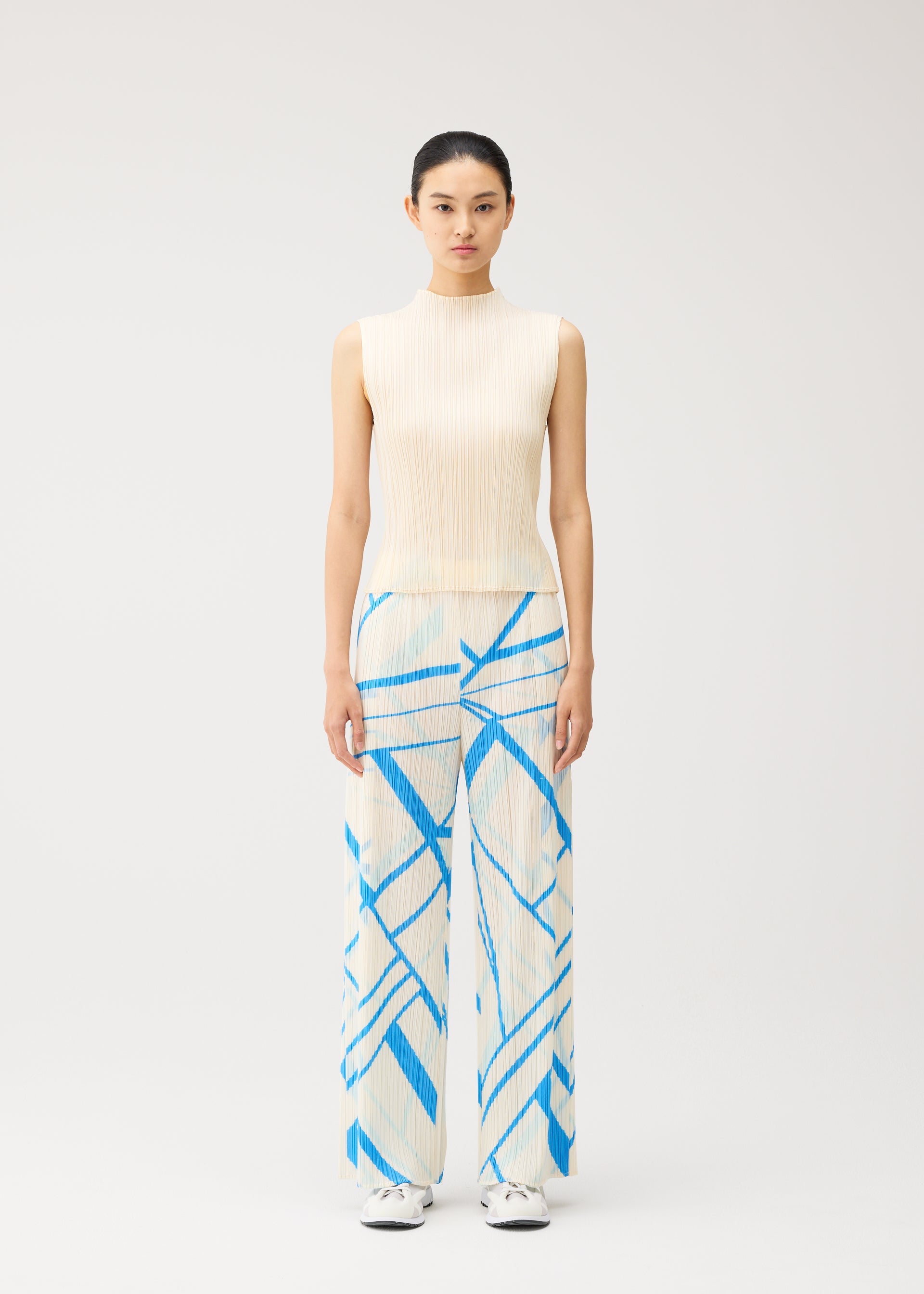 Zoomed view A woman stands facing forward, wearing the FOLD LINE sleeveless cream top and wide-leg trousers with a blue geometric pattern by PLEATS PLEASE ISSEY MIYAKE, featuring a minimalist design. Her hair is tied back, and she is wearing white shoes against a plain, light-colored background.