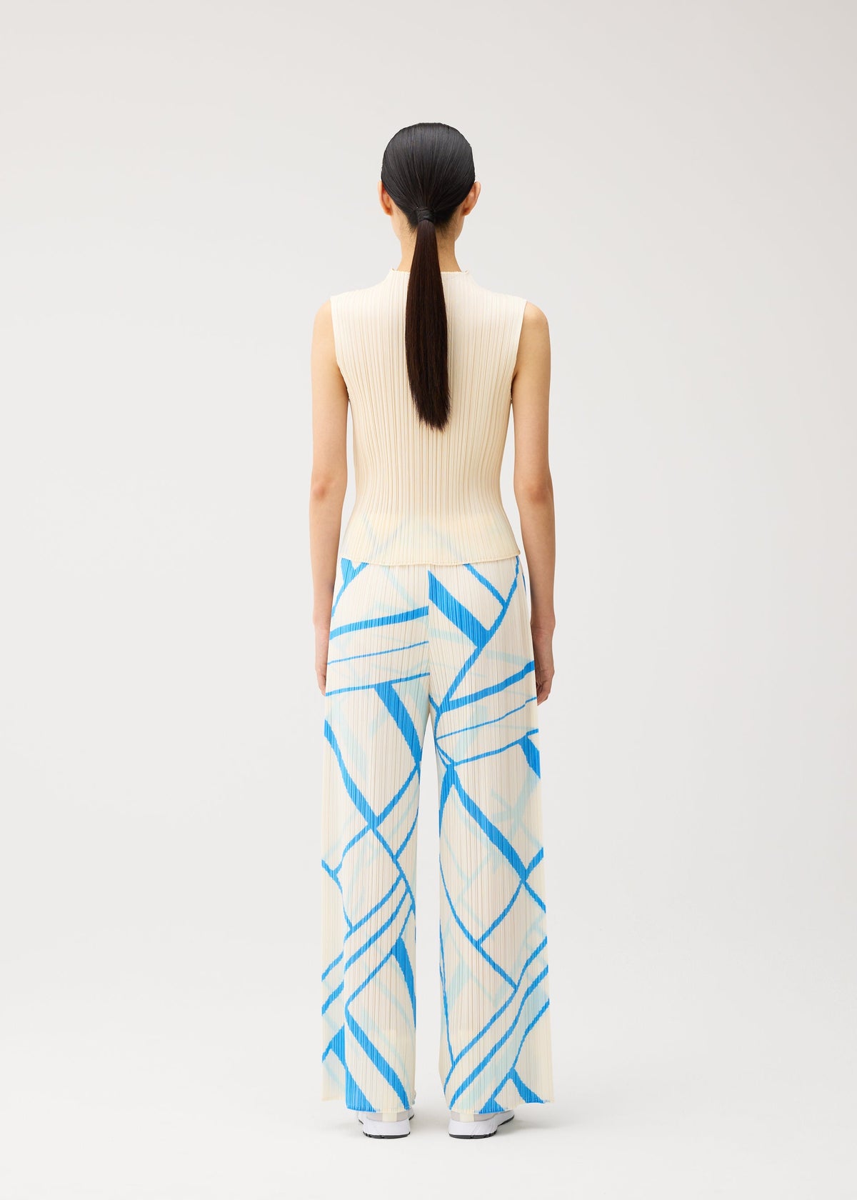 A person with long dark hair in a low ponytail is shown from behind, standing against a plain light background, dressed in the FOLD LINE ensemble by PLEATS PLEASE ISSEY MIYAKE—a sleeveless cream knit top and wide-leg cream pants adorned with minimalist blue geometric stripes. view 7 of 8