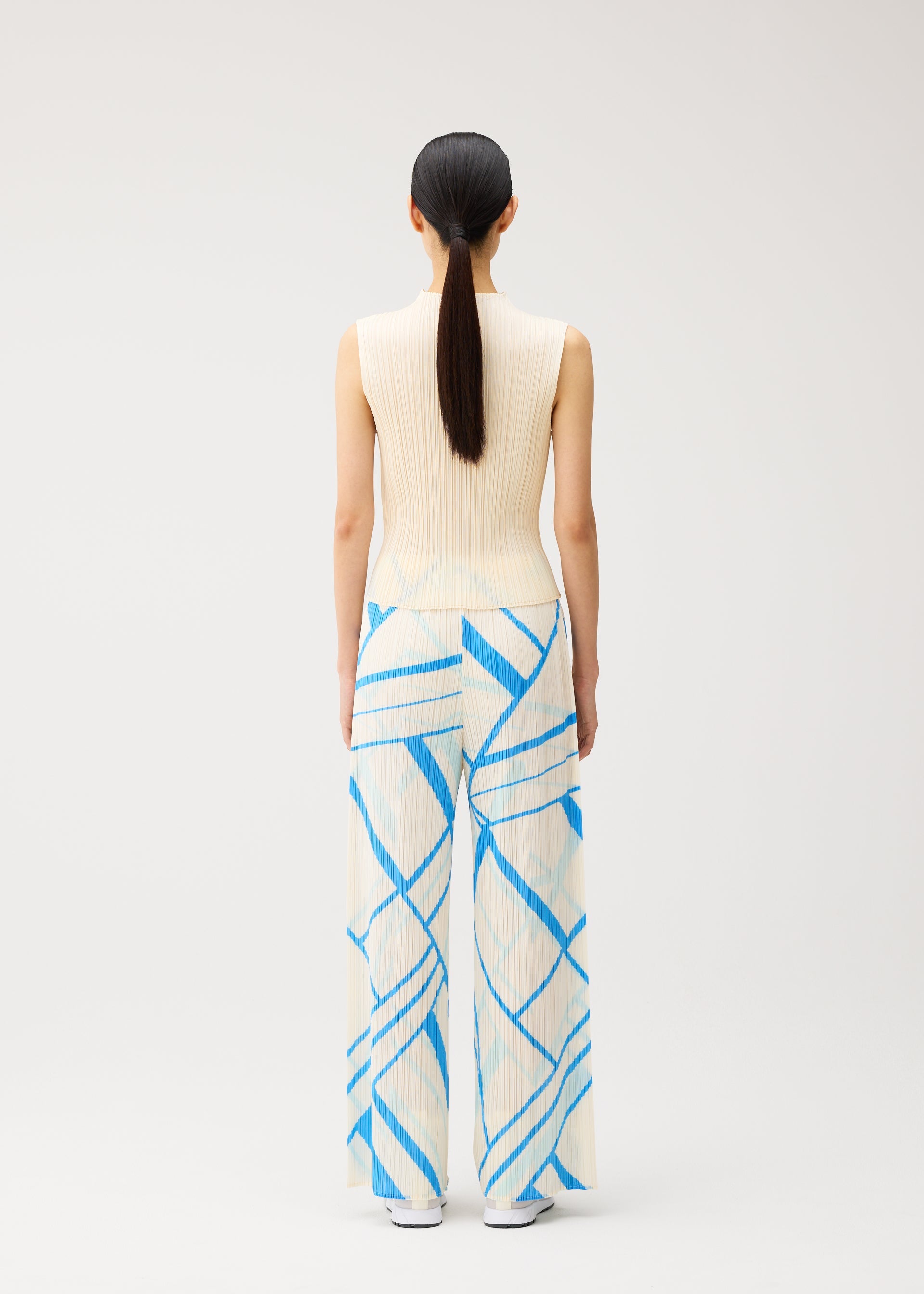 Zoomed view A person with long dark hair in a low ponytail is shown from behind, standing against a plain light background, dressed in the FOLD LINE ensemble by PLEATS PLEASE ISSEY MIYAKE—a sleeveless cream knit top and wide-leg cream pants adorned with minimalist blue geometric stripes.