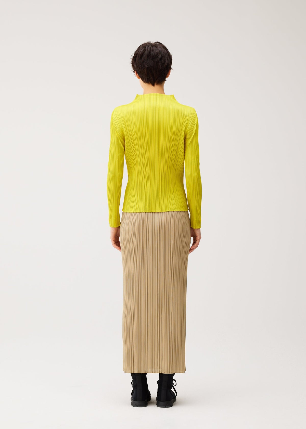 Zoomed view A person with short dark hair wears the MONTHLY COLORS : OCTOBER set by PLEATS PLEASE ISSEY MIYAKE—yellow long-sleeve top and beige pleated skirt with pockets—against a plain white background.