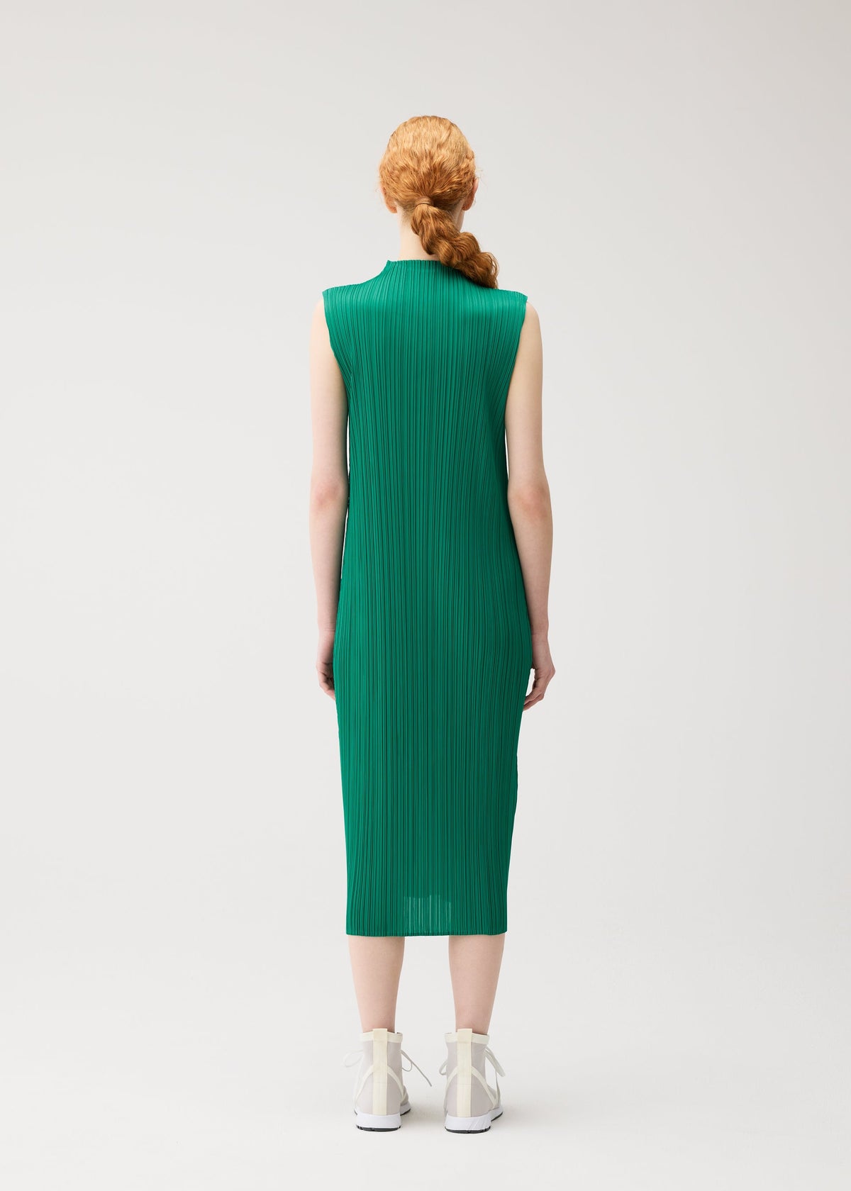 A person faces away from the camera, wearing the PLEATS PLEASE ISSEY MIYAKE MONTHLY COLORS : JULY sleeveless green high-neck dress with white high-top sneakers, standing against a plain white background. view 9 of 10