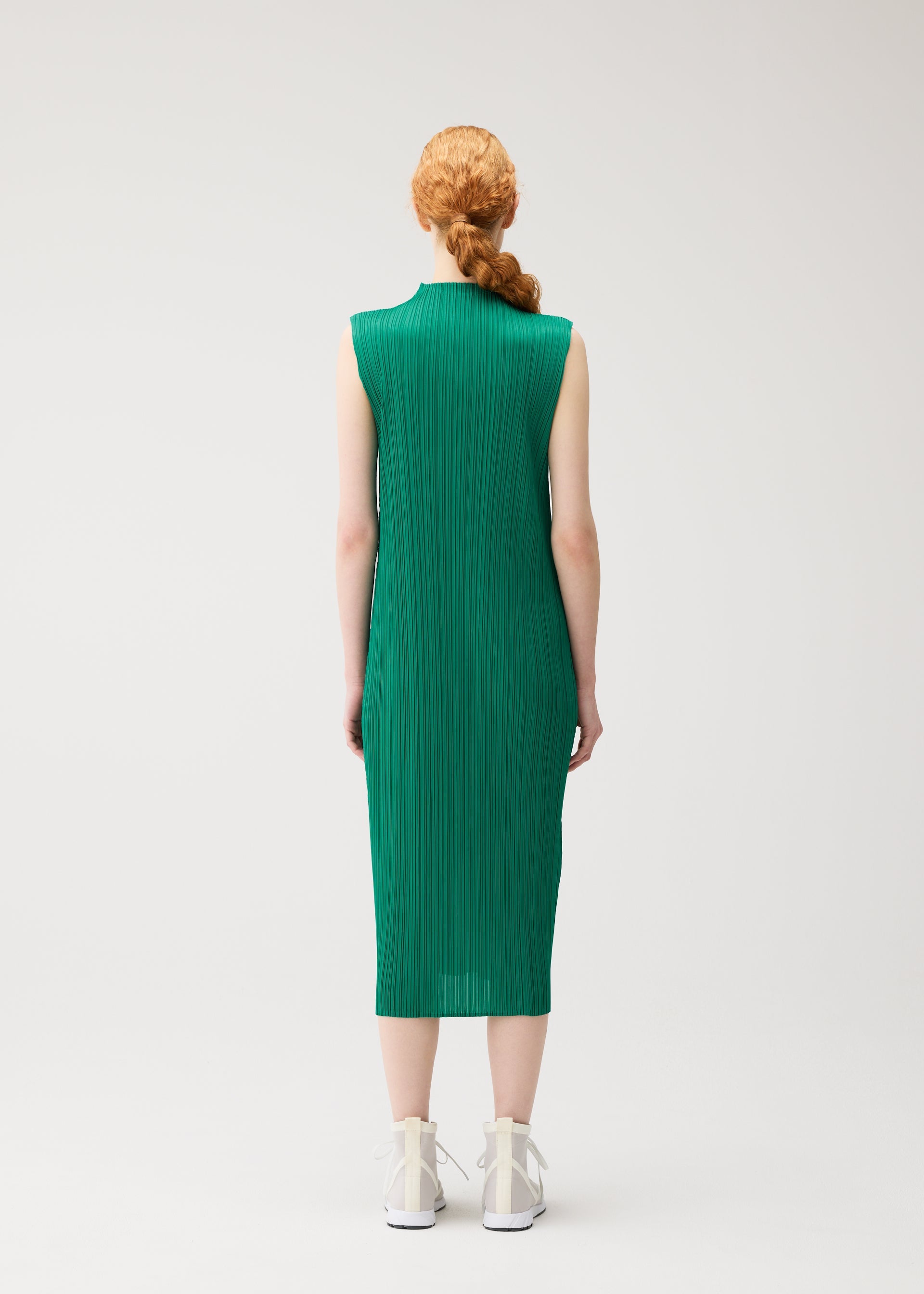 Zoomed view A person faces away from the camera, wearing the PLEATS PLEASE ISSEY MIYAKE MONTHLY COLORS : JULY sleeveless green high-neck dress with white high-top sneakers, standing against a plain white background.