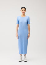 A woman stands facing forward, wearing the MONTHLY COLORS : AUGUST light blue, short-sleeved pleated midi dress by PLEATS PLEASE ISSEY MIYAKE with white high-top sneakers against a plain, light background.