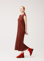 A woman wearing the PLEATS PLEASE ISSEY MIYAKE’s MONTHLY COLORS : SEPTEMBER round-neck sleeveless, ankle-length brown pleated dress in gentle tones and bright orange lace-up shoes stands sideways against a plain white background, capturing the subtle elegance of changing seasons.