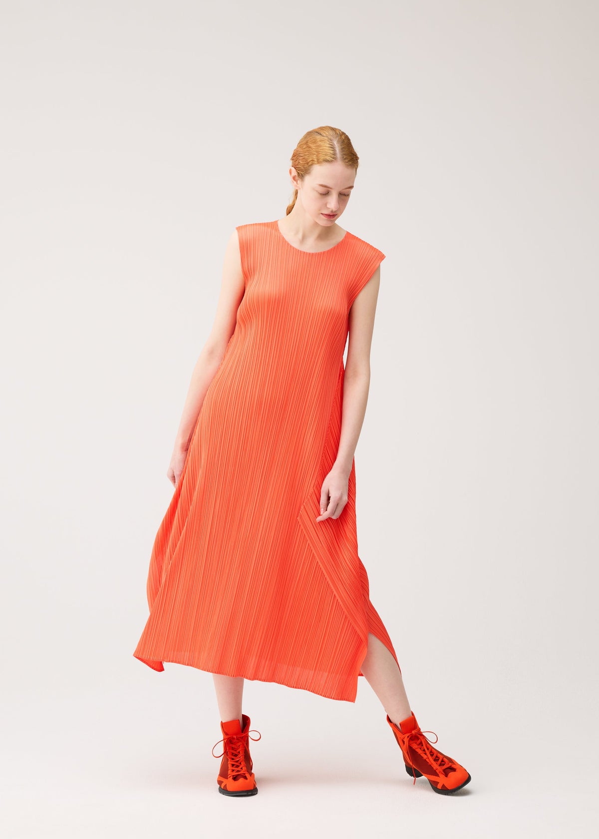 A person wearing the MONTHLY COLORS : SEPTEMBER sleeveless orange ribbed dress and matching orange boots from PLEATS PLEASE ISSEY MIYAKE stands against a plain light background, looking down with one leg bent and gently touching the dress. view 10 of 11