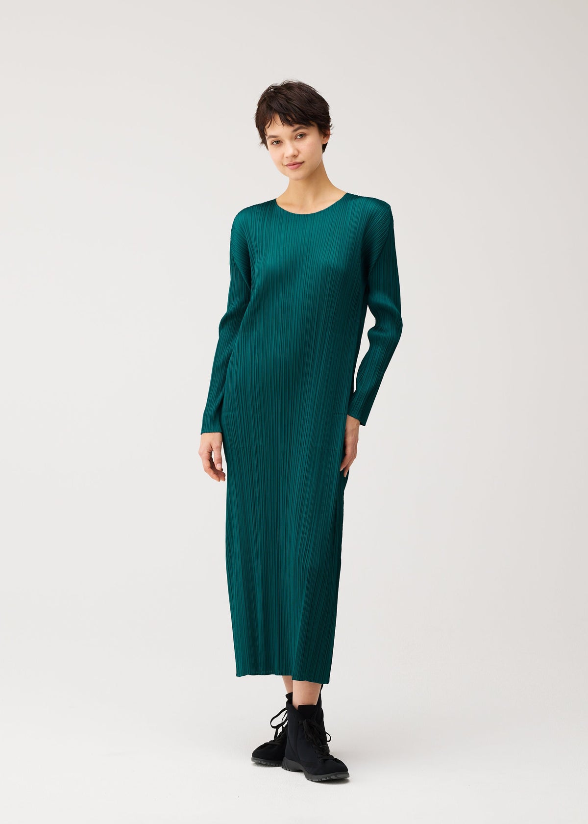 Zoomed view A person in the MONTHLY COLORS : OCTOBER dress by PLEATS PLEASE ISSEY MIYAKE and black lace-up boots stands against a plain light background.