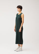 A person with short dark hair wears the PLEATS PLEASE ISSEY MIYAKE COTTON DENIM sleeveless, calf-length dress, paired with white high-top sneakers, standing sideways against a plain white background.