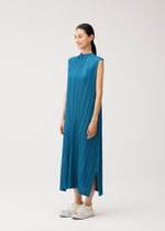 A person stands in the MELLOW PLEATS sleeveless blue pleated midi dress with pockets by PLEATS PLEASE ISSEY MIYAKE, paired with white sneakers, smiling and looking to the side against a plain light background.