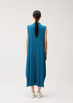 A person with long dark hair in a ponytail is seen from behind, wearing the ankle-length blue MELLOW PLEATS dress by PLEATS PLEASE ISSEY MIYAKE—a sleeveless, pleated design featuring pockets—paired with white sneakers, standing against a plain light background.