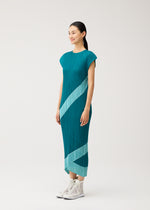 Wearing the TWIRL dress by PLEATS PLEASE ISSEY MIYAKE, a woman stands against a neutral backdrop. The teal midi dress features pleats, sleeveless styling, and light blue diagonal stripes, paired with white high-top sneakers.