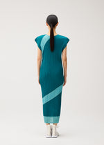 A woman with straight dark hair in a ponytail stands facing away, wearing the TWIRL dress by PLEATS PLEASE ISSEY MIYAKE—a teal, round-neck reversible style featuring light blue diagonal stripes—paired with white shoes, set against a plain light background.