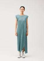 A woman stands facing forward, smiling, wearing the FOLD teal round-neck pleated midi dress with cap sleeves by PLEATS PLEASE ISSEY MIYAKE and white high-top sneakers against a plain white background.