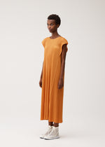 A person wears the BOUQUET dress by PLEATS PLEASE ISSEY MIYAKE, a floral-inspired loose-fitting orange piece with cap sleeves, paired with white high-top sneakers against a plain background.