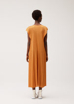 A person wearing the BOUQUET orange midi dress by PLEATS PLEASE ISSEY MIYAKE with white shoes faces away from the camera against a plain, light background.