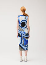 A person with long, curly red hair in a ponytail stands facing away, wearing the PLEATS PLEASE ISSEY MIYAKE ROLL sleeveless, knee-length printed dress with an abstract blue, black, and white pattern and white high-top shoes against a plain background.