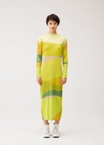 A person stands facing forward in the ORBIT dress by PLEATS PLEASE ISSEY MIYAKE—long-sleeved, yellow and green geometric print—paired with white lace-up boots against a plain light background.