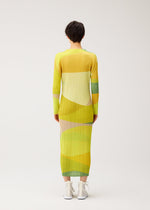 A person with short dark hair wears the ORBIT long-sleeved dress by PLEATS PLEASE ISSEY MIYAKE, featuring sheer yellow, green, and beige abstract patterns, paired with white ankle boots against a plain light background.