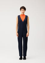 A person stands against a plain light background wearing PLEATS PLEASE ISSEY MIYAKE’s THICKER BOTTOMS 2—a sleeveless navy V-neck jumpsuit with pockets and thick fabric—styled over an orange high-neck top and black shoes.